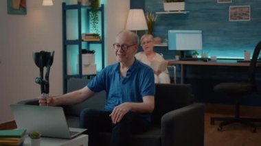 İnternetteki konferansta ailesiyle konuşmak için dizüstü bilgisayar kullanan koltuk değnekli yaşlı adam.