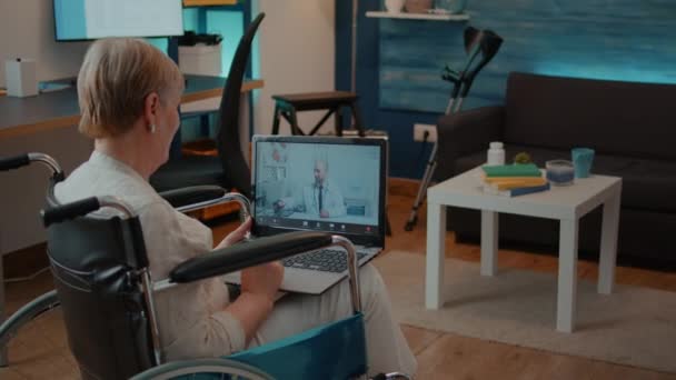 Oudere vrouw in een rolstoel met behulp van video bellen om te praten met de arts — Stockvideo