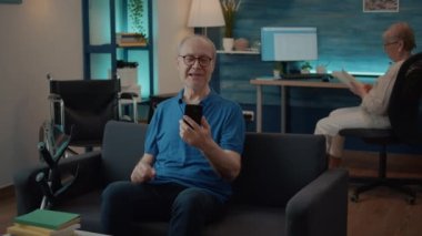 Ailesiyle görüntülü konuşma yapmak için elinde akıllı telefon tutan emekli adam.