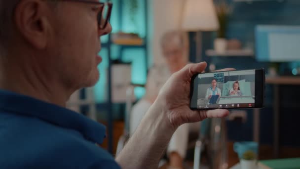 Pensionista sosteniendo smartphone para usar videoconferencia remota — Vídeos de Stock