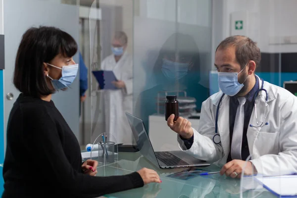 Patient and doctor with face mask talking about bottle of pills — Stock Photo, Image