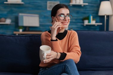 Kanepede gülümseyen, akıllı telefondan mutlu bir telefon görüşmesi yapan..