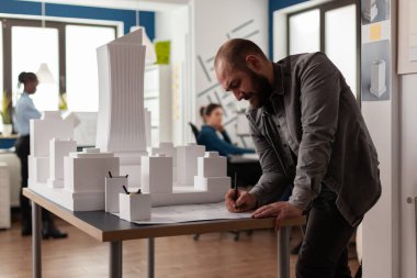 Modern mimarlık bürosundaki masanın üzerine planlar çizen mimar