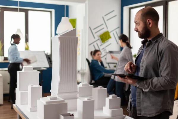 Arkitekt innehav tablett med ritningar inspektera design av vitt skum byggnad modell — Stockfoto