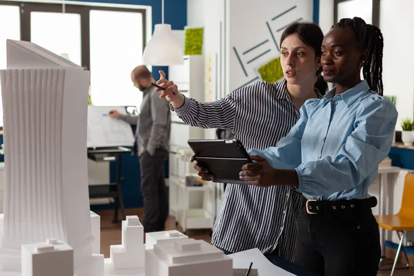 Arquitecta señalando lápiz a modelo arquitectónico rascacielos de pie junto a colega ingeniero — Foto de Stock