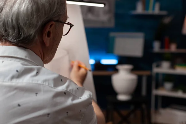 Concentre-se em artista aposentado desenhando esboço em papel usando lápis olhando para o modelo de vaso branco de gesso — Fotografia de Stock