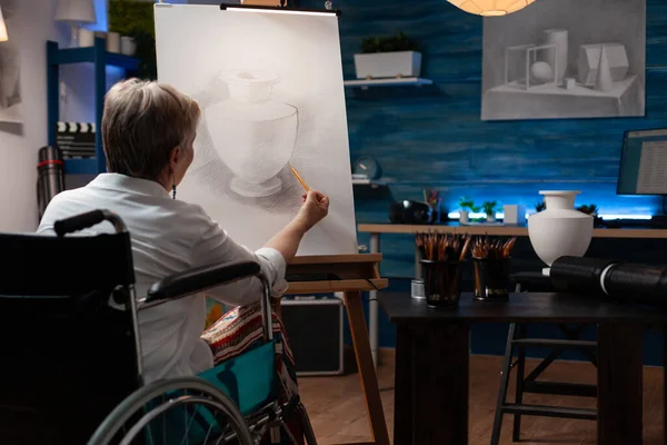 Fokuserad pensionerad konstlärare med hjälp av rullstol gör kreativa konstverk i penna teckning vas modell — Stockfoto