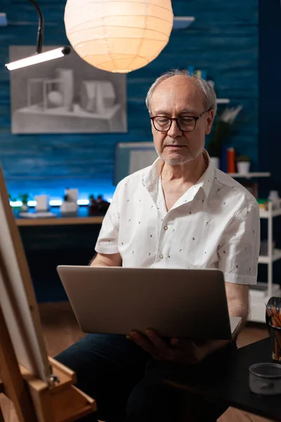 Πορτρέτο του ηλικιωμένου άνδρα που ψάχνει να πουλήσει έργα τέχνης στο διαδίκτυο χρησιμοποιώντας φορητό υπολογιστή — Φωτογραφία Αρχείου