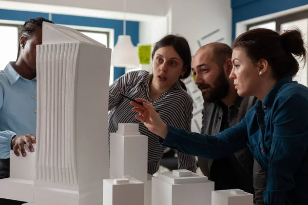 Professioneller Architekt mit Arbeitspartnern zeigt auf Schaumstoffmodell eines Wolkenkratzers — Stockfoto
