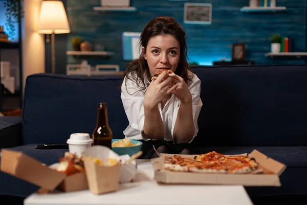 Persoon zittend op de bank in de woonkamer met een stuk pizza tijdens het kijken naar televisie sitcom — Stockfoto