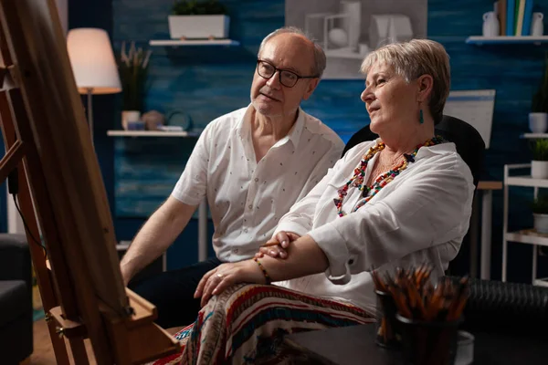 Senior couple looking at drawing sitting down in front of easel admiring creation — Stock Photo, Image
