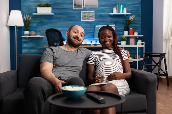 Feliz casal multirracial desfrutando de televisão e esperando bebê em casa — Fotografia de Stock