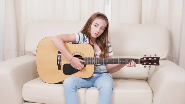 Joven guitarrista niño sentado en el sofá sosteniendo la guitarra aprendiendo a cantar — Foto de Stock