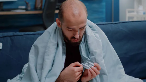 Крупный план больного человека, смотрящего на капсулы таблетки на столе — стоковое фото