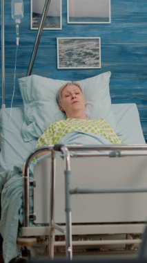 Hastalıklı yaşlı kadın kocasıyla konuşurken yatakta dinleniyor.