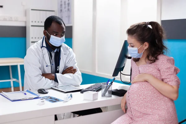 Médico afro-americano falando com mulher grávida na mesa — Fotografia de Stock