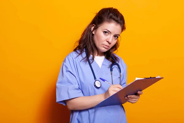 Infirmière avec uniforme prenant des notes sur des dossiers de presse-papiers — Photo