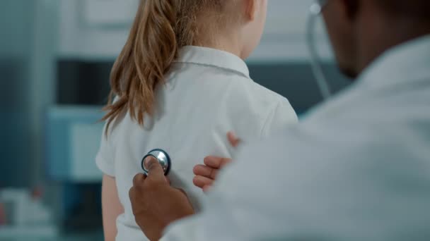 Médico afroamericano consultando a un niño pequeño con estetoscopio — Vídeos de Stock