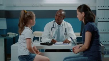 Doktor hastalarla konuşuyor ve bilgisayardan notlar alıyor.