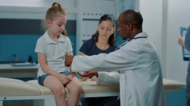 Yaralı kollu çocuğa sargı bezi uygulayan erkek doktor.