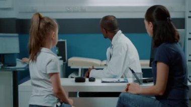 Afrikalı Amerikalı sıhhiyeci bir kızla annesine bir şişe hap veriyor.