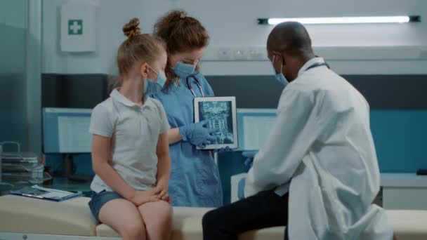 Різноманітна медична команда пояснює діагноз сканування рентгенівського променя маленькій дівчинці — стокове відео