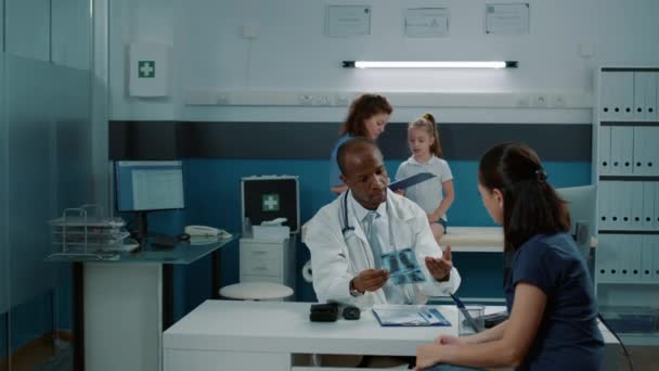 Профессиональный врач, объясняющий матери результаты рентгена на приеме — стоковое видео