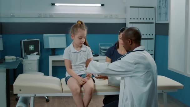 Врач общей практики накладывает повязку на сломанную руку маленькой девочки — стоковое видео