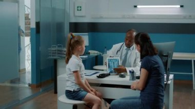 Anne ve çocuğa radyografi teşhisi koymak için elinde tablet olan doktor.