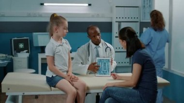 Doktor, küçük çocuk ve anneye radyografi sonuçlarını açıklıyor.