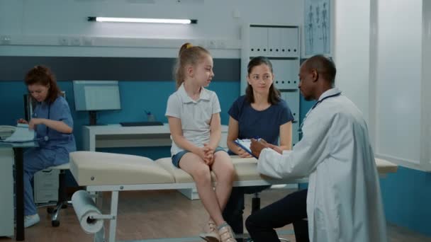Arzt macht Notizen auf Klemmbrettpapieren, um Kind zu untersuchen — Stockvideo