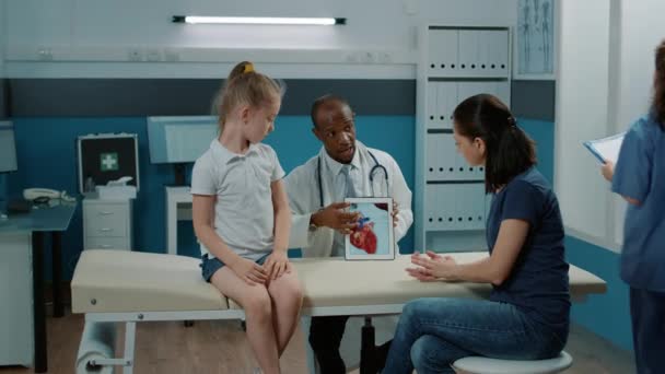 Медик показывает кардиологический диагноз на таблетках матери и ребенку — стоковое видео
