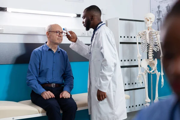 Afrikansk amerikansk läkare sätta infraröd termometer på gamle man patient foredhead — Stockfoto
