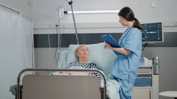 Läkarassistent besöker äldre kvinna med sjukdom i sängen — Stockfoto