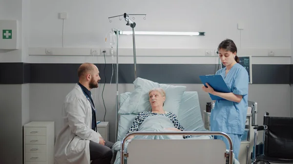 Ärzteteam berät alte Patientin im Bett — Stockfoto