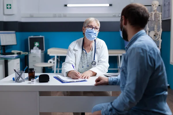 Medic doet overleg met zieke man tijdens covid 19 pandemie in het kantoor — Stockfoto