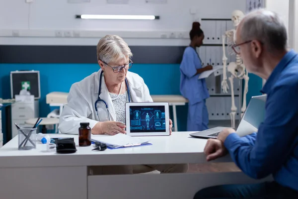 Sanitäter zeigt Seniorin Tablette mit Darstellung der menschlichen Körperanalyse — Stockfoto