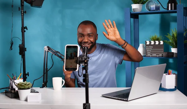 Creador de contenido haciendo gesto de la mano de saludo delante de la configuración de podcast de vídeo en vivo sentado en el escritorio — Foto de Stock