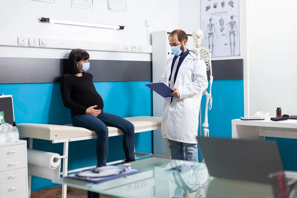 Tıbbi kabinedeki hamile kadına danışan yüz maskesi uzmanı. — Stok fotoğraf