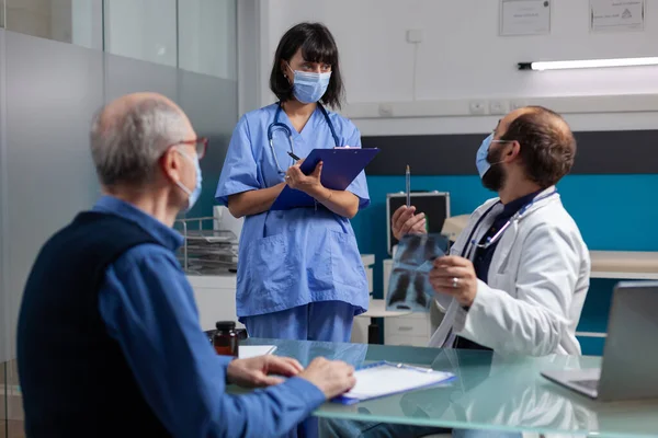 Arzt spricht mit Krankenschwester und hält Röntgenbild bei Kontrollbesuch — Stockfoto