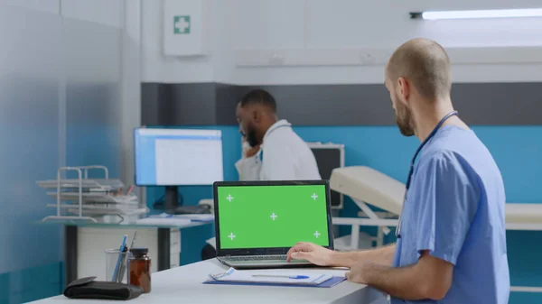 理疗师护士坐在桌旁，在模拟绿色屏幕彩色关键笔记本电脑上打字，具备疾病专业知识 — 图库照片