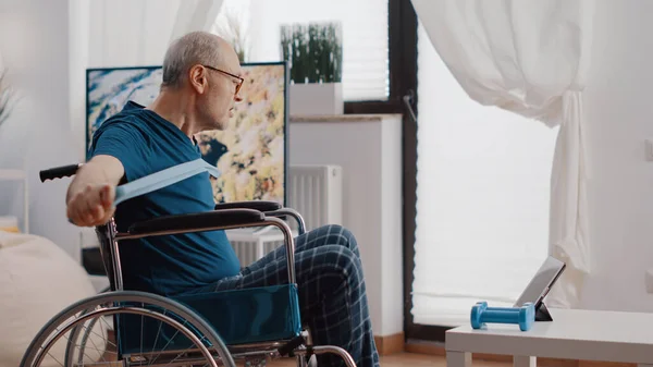 Homem aposentado sentado em cadeira de rodas e usando banda de resistência — Fotografia de Stock