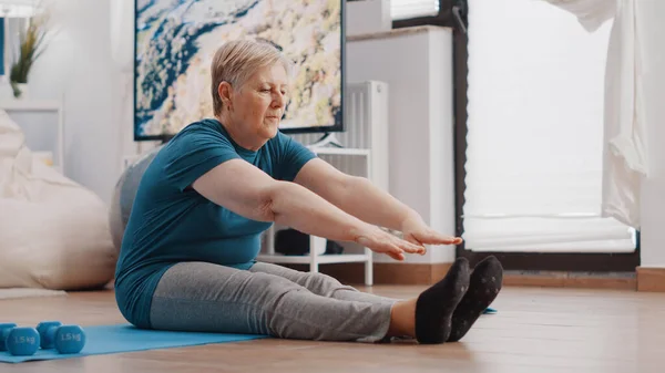 Aged woman doing stretching exercise on yoga mat