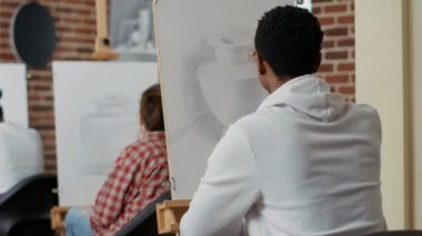 Genç öğrenci tuvale çizim yapmak için vazo modeline bakıyor.