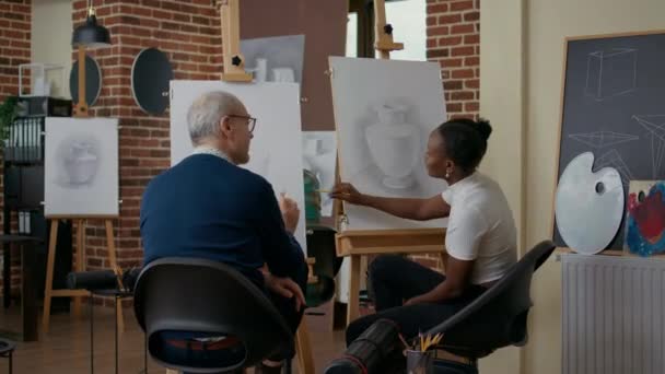 Nő elmagyarázza az idősebb férfinak, hogyan rajzoljon modellt a vászonra — Stock videók
