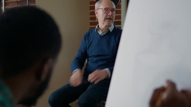 Anciano artista enseñando a la gente en la clase de arte a dibujar una obra maestra sobre lienzo — Vídeos de Stock