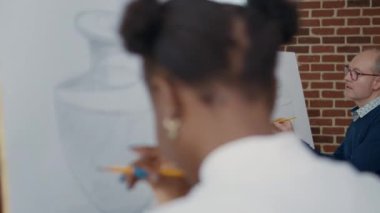 Resim dersinde tuvale resim çizen yaşlı bir adam ve kadın.