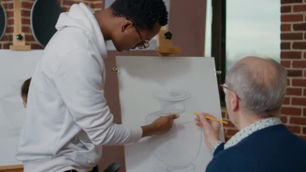 Joven artista explicando la técnica de dibujo a la persona mayor — Vídeos de Stock