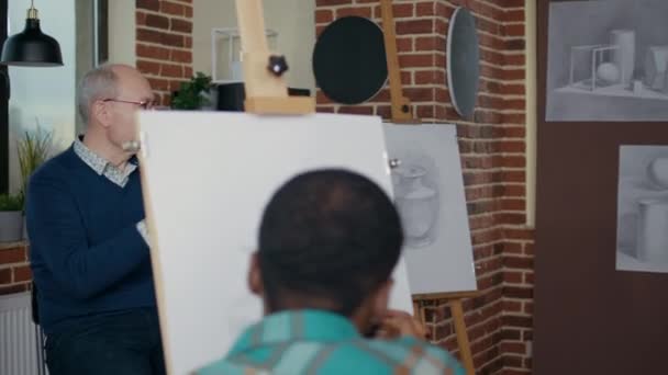 Hombre mayor enseñando a las personas en clase de arte a dibujar sobre lienzo — Vídeos de Stock