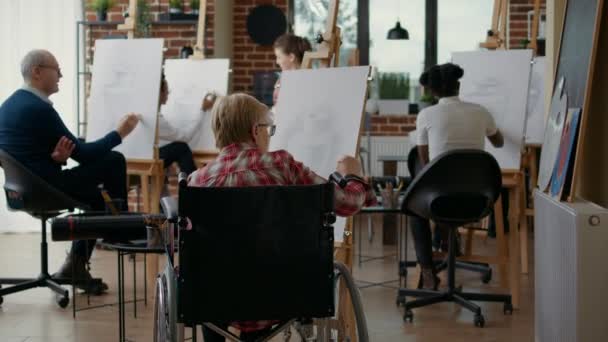 Mulher idosa com deficiência frequentando aula de arte com jovem artista — Vídeo de Stock